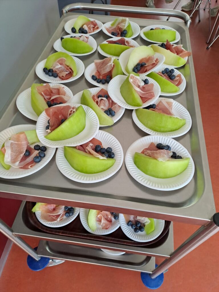 trolley met veel witte bordjes met een stuk meloen, rauwe ham en blauwe bessen